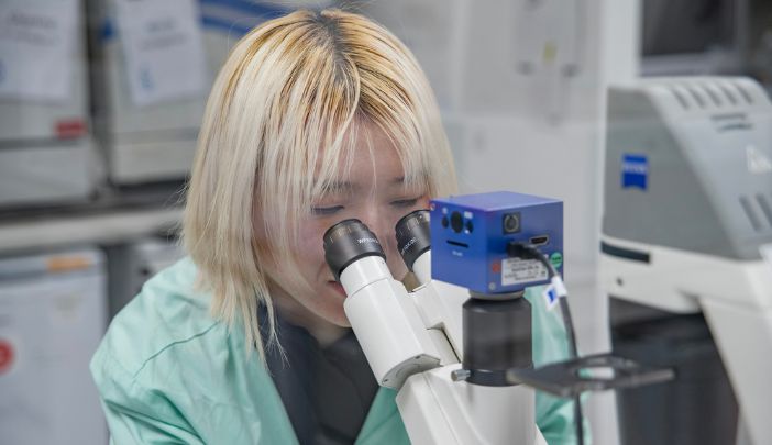 A postgraduate research wearing a lab coat looks into a microscope
