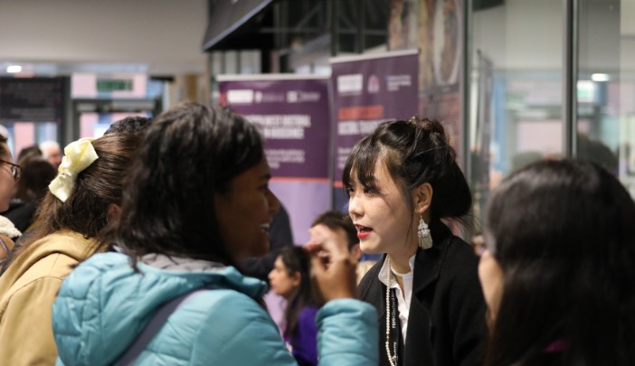 A staff member talking to a prospective researcher at a busy open day