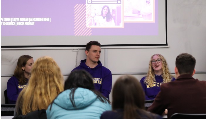 Three current postgraduate researchers sat in front of a screen with event attendees watching