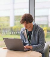 A male postgraduate researcher sits intently typing at a laptop. 