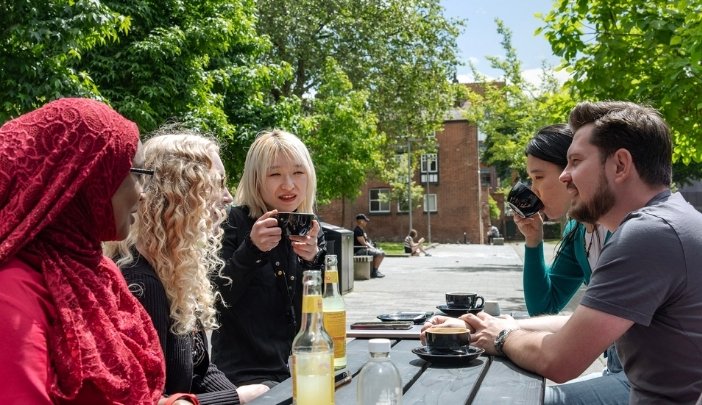 A group of postgraduate researchers sit at a table outside chatting over a coffee and drinks