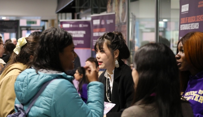 A Chinese member of staff talks to prospective applicants at a busy open day.