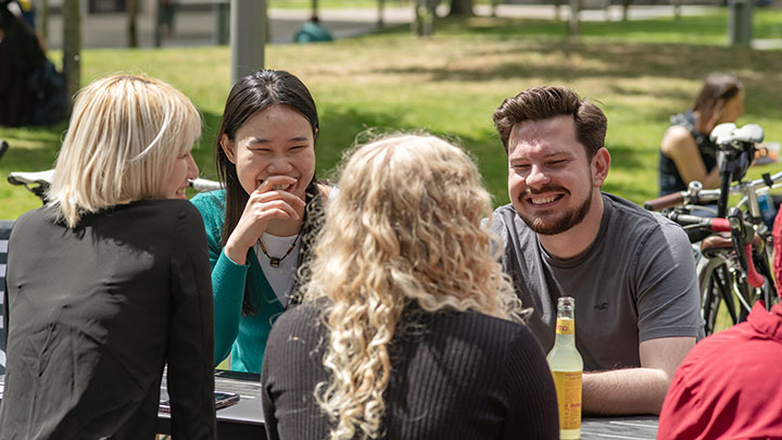 Postgraduate research students sitting together on a picnic bench in a green space.