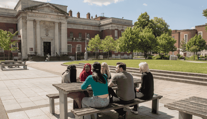 A group of researchers sit at a bench in the sun near the Samuel Alexander Building