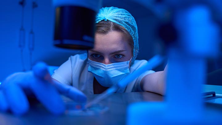 A researcher reaching across a lab bench to add a sample to a petri dish.