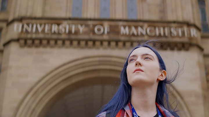 Portrait of a woman standing outside of a building with The University of Manchester written on it.