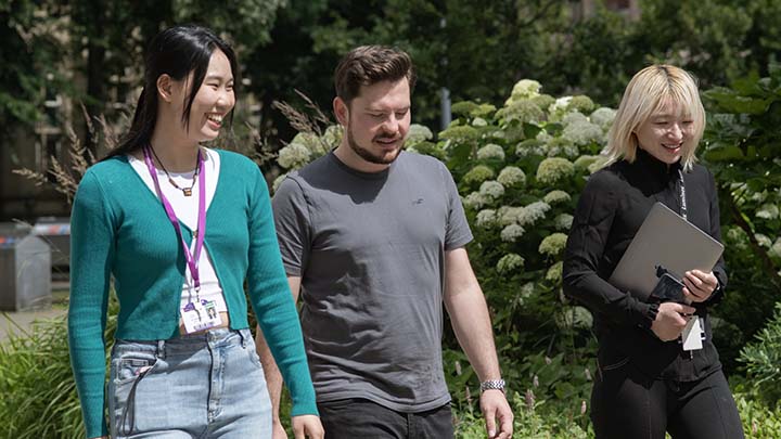 A group of three postgraduate students walking through the Manchester campus.