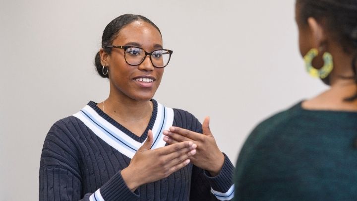 A postgraduate researcher smiling gesturing with their hands in front of another student 