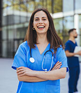 A young female doctor in blue scrubs laughing in an outdoor setting.
