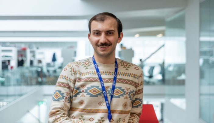 A male researcher in a jumper smiles looking at the screen