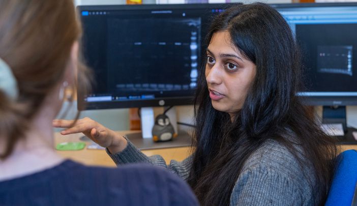 Dhruti, a PhD student, sat at a computer talking to a colleague
