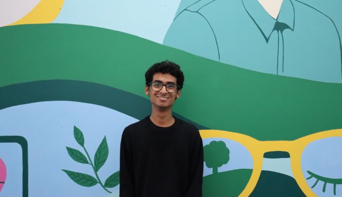 Postgraduate researcher Aadhi smiling at the camera in front of a colourful wall display