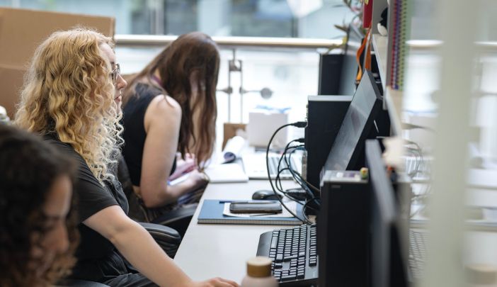 Postgraduate researcher Holly working on a computer in a busy computer lab.