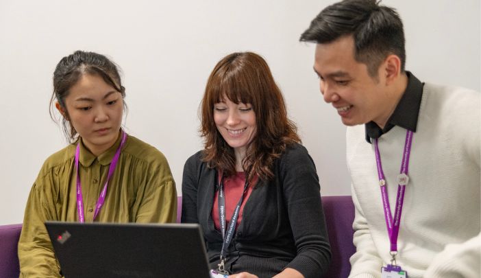Two postgraduate researchers smiling, sitting either side of a member of a support team