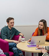 Two students working on a laptop together in a relaxed setting.