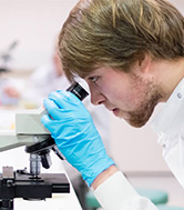 A Doctor using a microscope, wearing blue gloves.