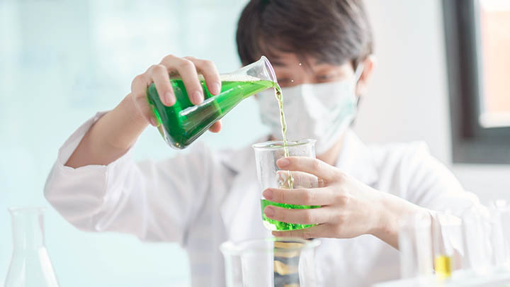 A student pours a green liquid from a flask into a beaker.